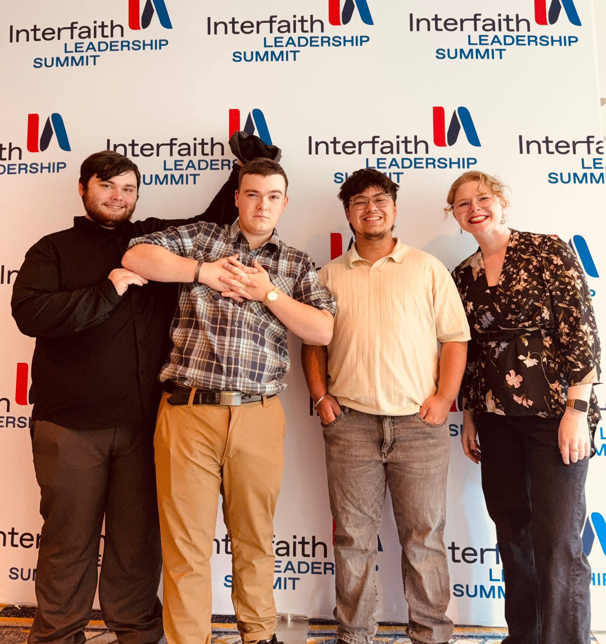 Kaufman Interfaith Institute's Rachel Robinson and three GVSU students pose in front of an Interfaith America branded backdrop